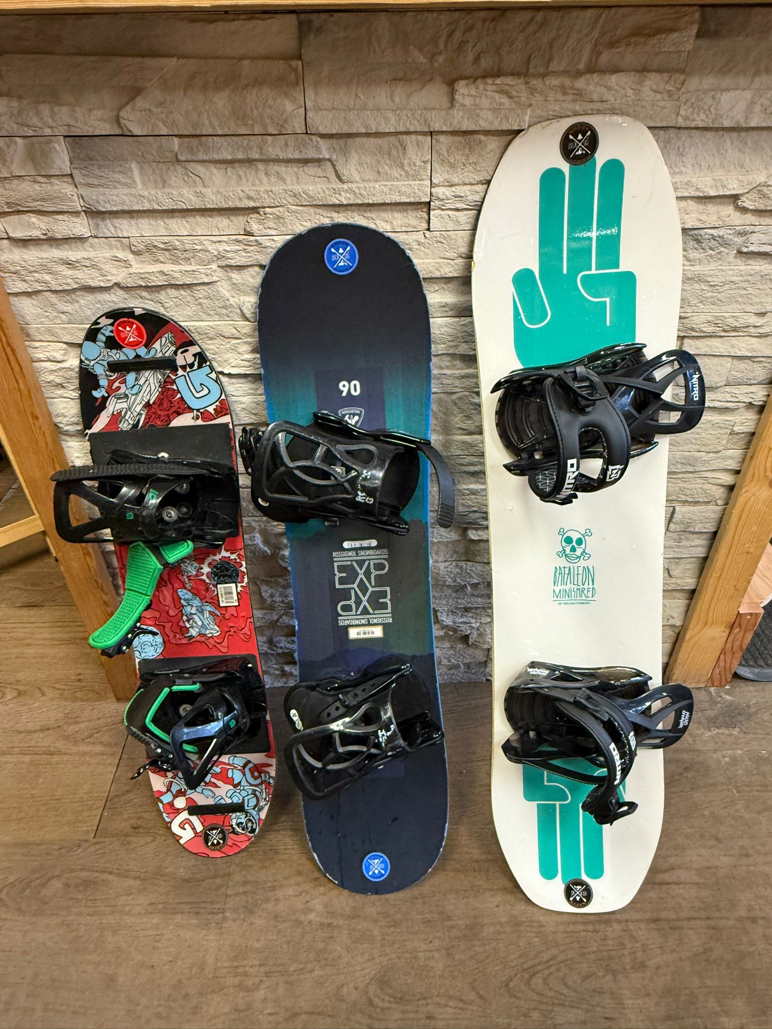 Three Rossignol and Bataleon children's snowboards leaning against a wall