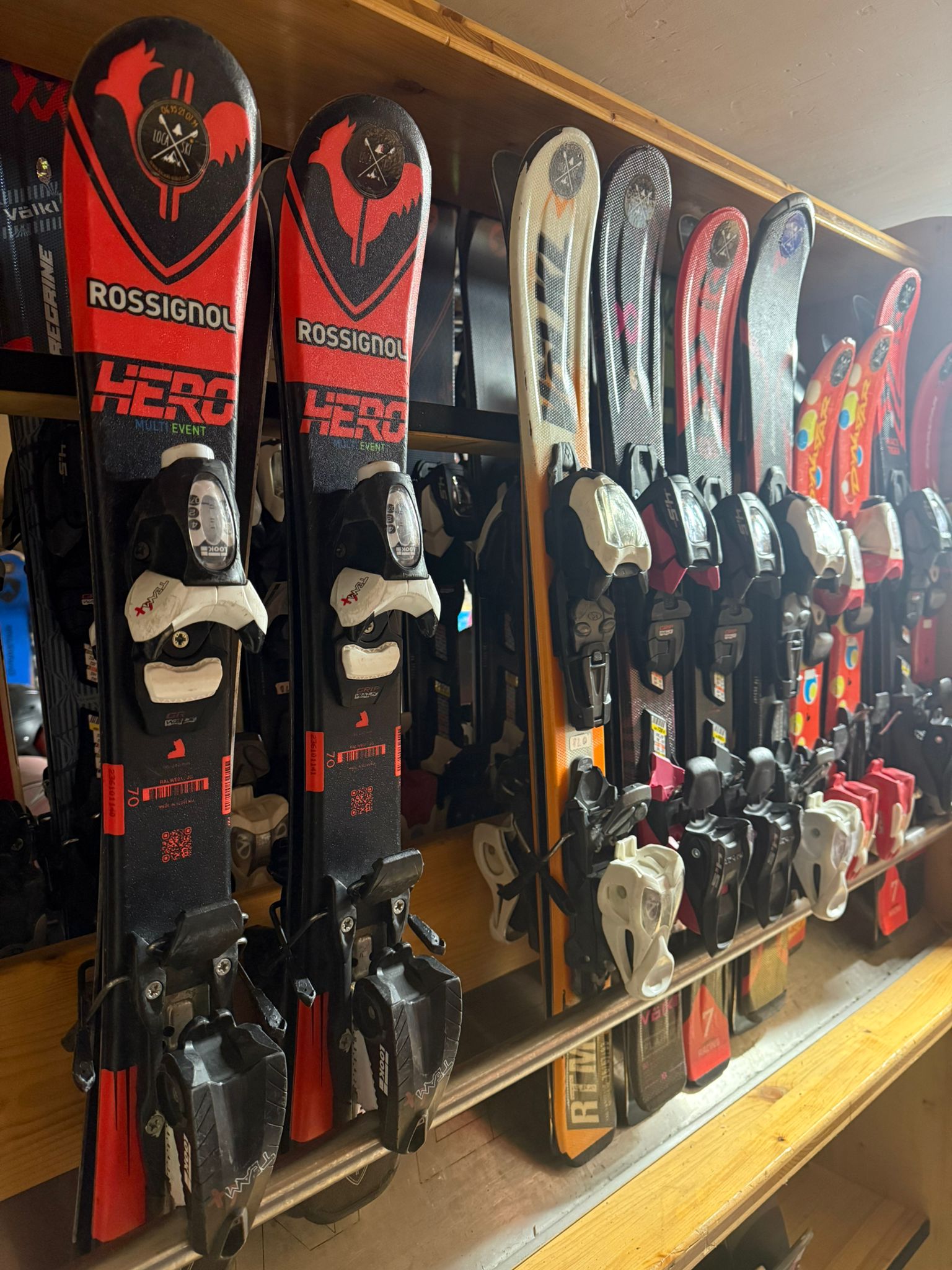 Alignment of red and black Rossignol Hero skis on a wooden rack at Loca'ski