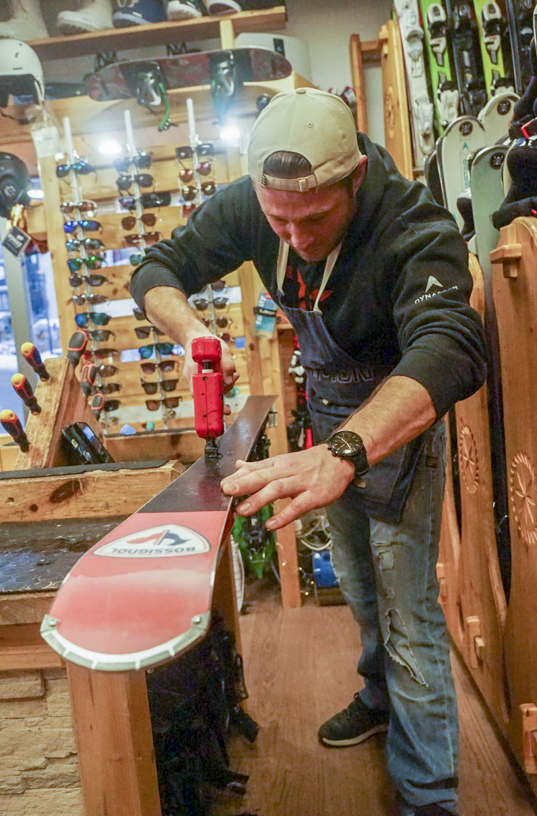 Mountain workshop technician performing maintenance on the base of a Rossignol ski with a professional repair tool.