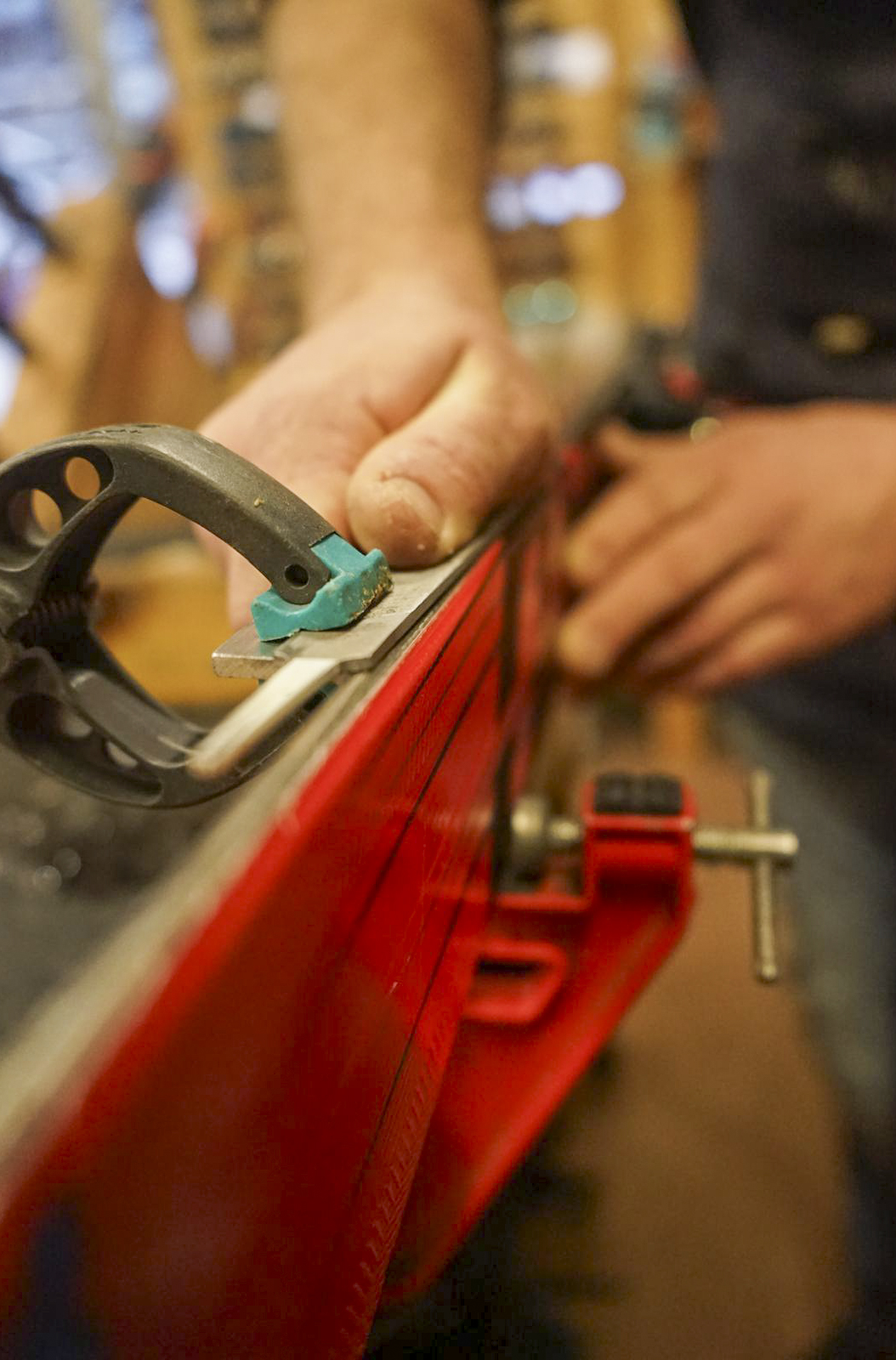 Manual edge sharpening of a red ski held in a vice within a specialized workshop.