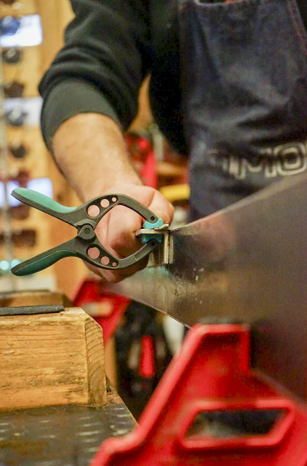 Technician performing maintenance and edge sharpening of a ski using a clamp in a professional workshop.