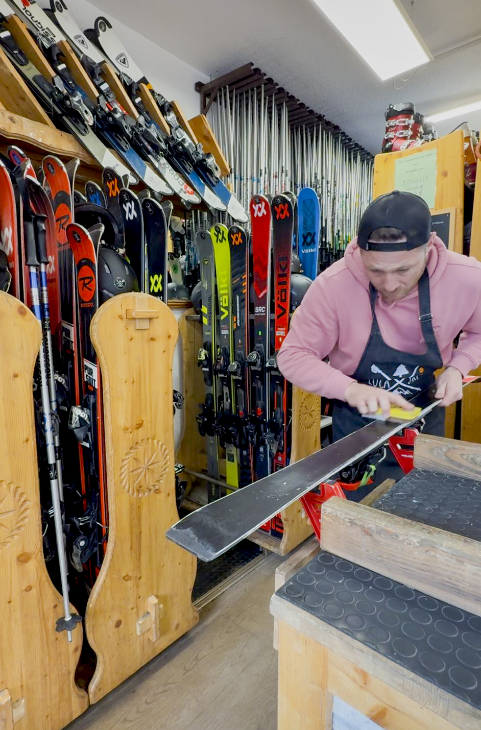 Ski technician performing manual waxing of an alpine ski in a professional repair workshop.