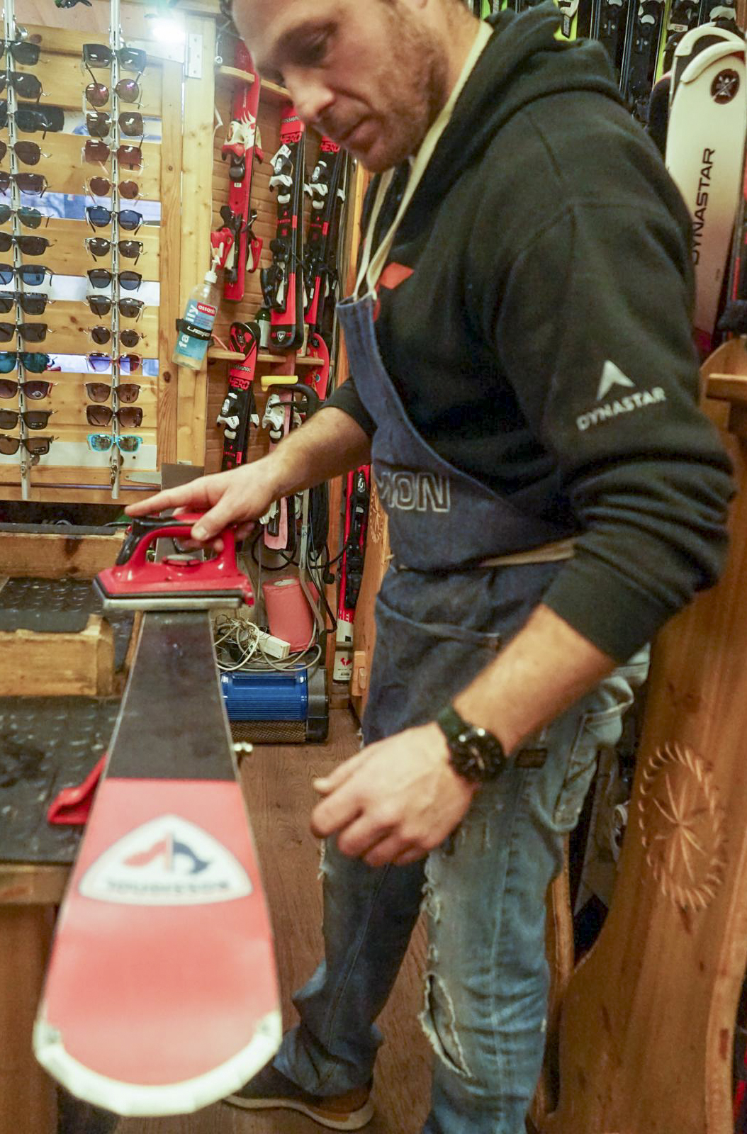 A technician maintains a ski using a red waxing iron in a winter sports workshop.